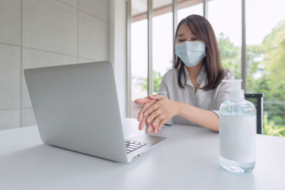 Young woman using sanitizer while sitting on table