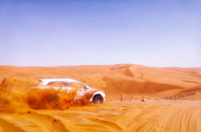 Car on desert land against clear sky