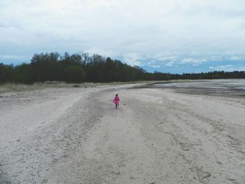 Rear view of girl sunning at beach against cloudy sky