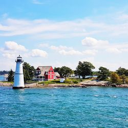 Lighthouse amidst sea and buildings against sky