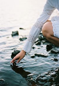 Midsection of woman touching water in sea