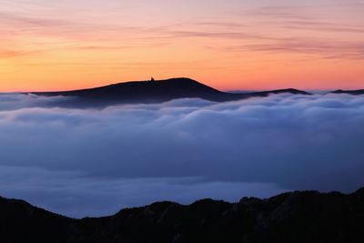 Scenic view of dramatic sky over silhouette mountains during sunset