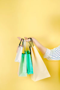 Cropped hand holding shopping bags against yellow background
