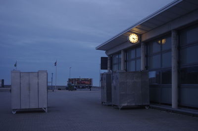 Illuminated street by building against sky at dusk