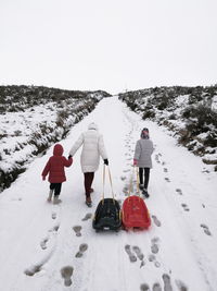 Rear view of family with sled walking on snow covered field against clear sky