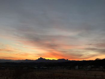 Scenic view of silhouette field against dramatic sky during sunset