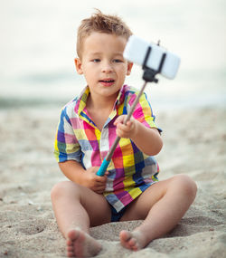 Boy taking selfie with smart phone while sitting on beach