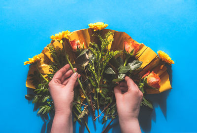 Close-up of hand holding yellow flower against blue sky