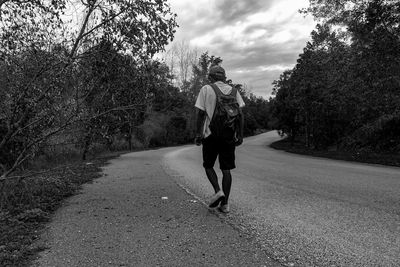 Man walking on road amidst trees against sky