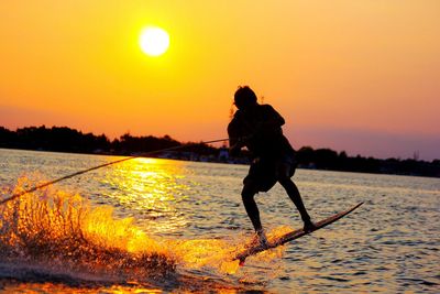 Man waterskiing on sea against orange sunset sky