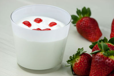 Close-up of strawberries by yogurt against white background