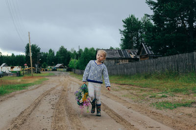 Girl in casual clothes walks through the village with a basket of wildflowers