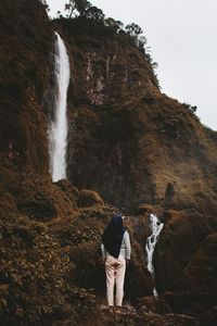 Rear view of woman standing on rock against waterfall