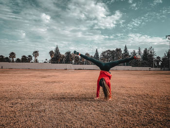 Full length of young woman doing handstand on field against sky