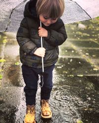 Full length of boy holding umbrella standing in rain