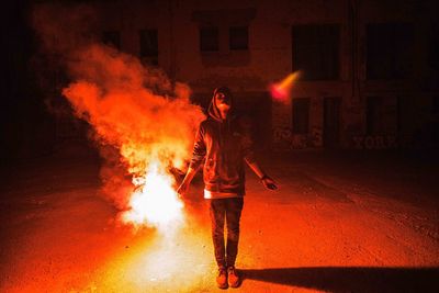 Man looking up while holding red burning flare at night on street