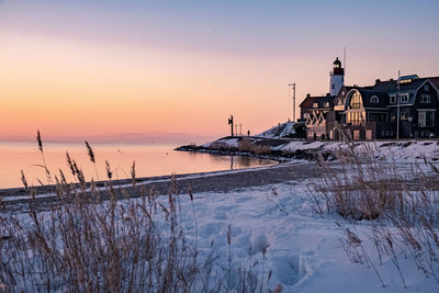 Frozen sea by buildings against sky during sunset