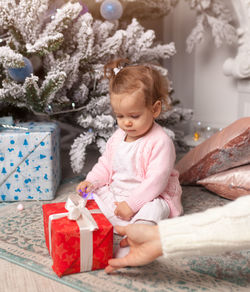 Cropped image of mother giving christmas gift to girl sitting at home