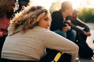 Thoughtful woman sitting with friends at skateboard park