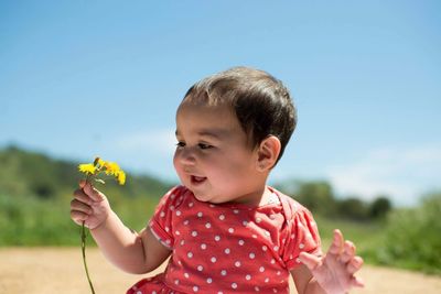Smiling girl holding yellow flowers against sky