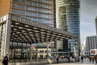 People walking on road by modern buildings in city