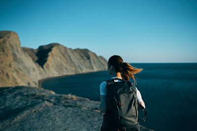 Rear view of woman standing on beach against clear blue sky