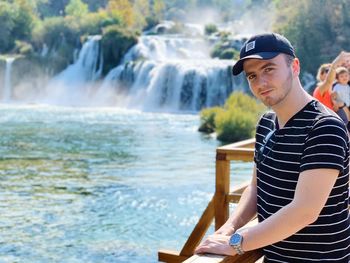 Portrait of young man standing against waterfall