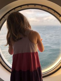 Rear view of woman looking out a circular window at sea against sky