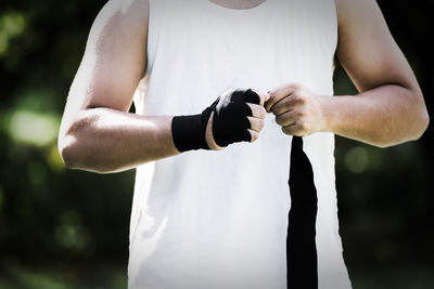 Midsection of boxer tying bandage while standing outdoors