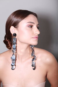 Indoor head shot of brunette model wearing long shiny earrings, professional make up tied hairstyle