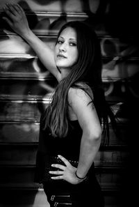 Side view portrait of young woman with hand on hip standing by shutter