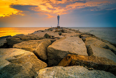 Lighthouse by sea against sky during sunset