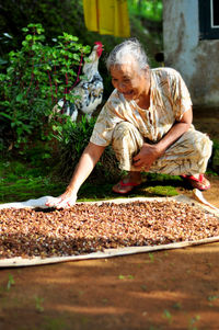 Full length of senior woman drying cloves while crouching by plants at yard