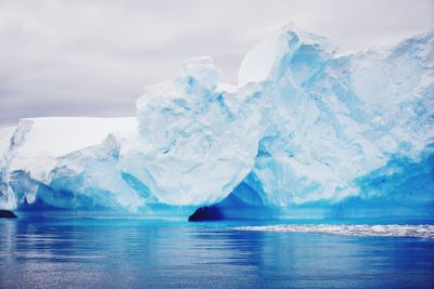 Scenic view of iceberg in sea against cloudy sky