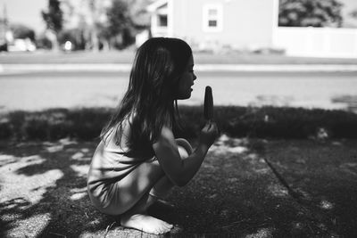 Side view of girl having popsicle on footpath during sunny day