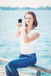 Young woman taking selfie with mobile phone against sea