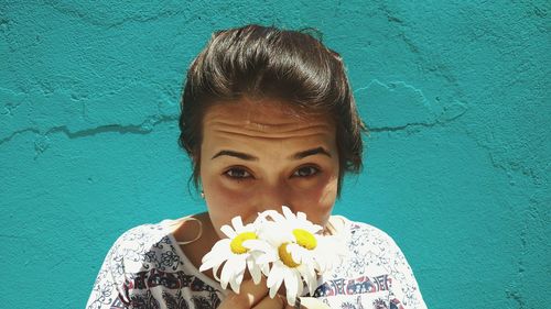 Portrait of woman holding flower against blue wall