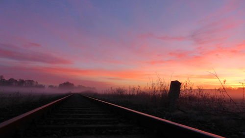 Railroad tracks on field against sky during sunset