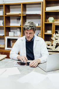 Craftsman wearing lab coat using tablet pc in workshop