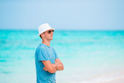 Man wearing hat standing at beach against sky