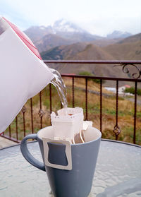 Hot water being poured into the portable drip coffee bag with blurry countryside view in background