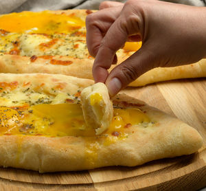 Baked adjarian khachapuri with whole egg yolk on a wooden board, hand beats a piece of bread 