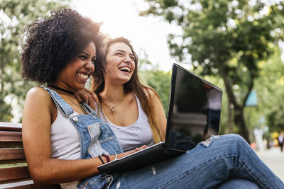 Female friends using laptop while sitting on bench