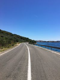 Road by sea against clear blue sky