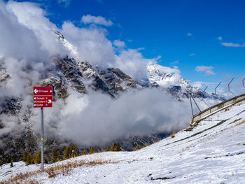 Road sign on snow covered mountain against sky