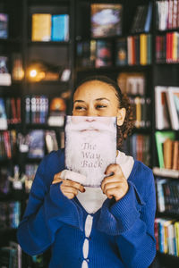 Young woman holding book near face in bookstore