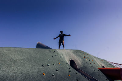 Low angle view of man skateboarding on skateboard against clear blue sky