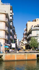 Buildings by river against clear blue sky