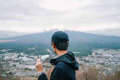 Side view of man wearing cap eating ice cream against mountain and sky