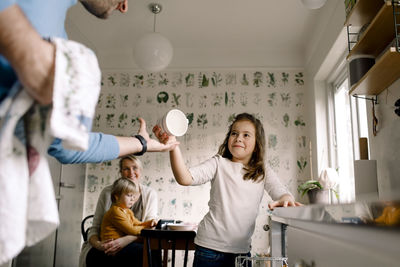 Smiling daughter giving cup to father in kitchen at home